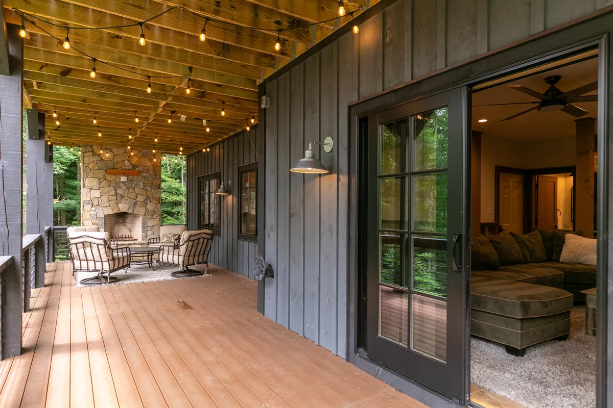 A cozy outdoor living space featuring a large stone fireplace surrounded by comfortable seating, illuminated by string lights as dusk falls. The setting is intimate, framed by trees and perfect for gatherings or quiet reflection under the stars.