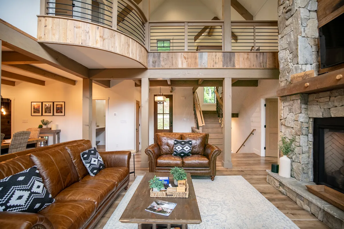 This image showcases a welcoming loft-style space with a stone fireplace, a brown leather sofa, wooden railing balcony, and a dining table with chairs. Natural light streams through the windows, and the open design offers a glimpse of the peaceful, inspiring atmosphere described in the section.