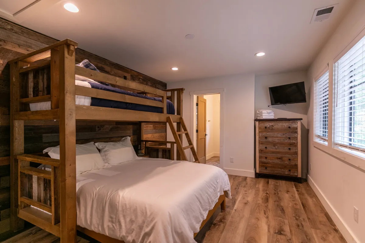 A spacious suite featuring a queen bed and a bunk bed, with a large window allowing natural light to fill the room. The wooden dresser and relaxed layout make it perfect for families or groups seeking comfort and privacy.