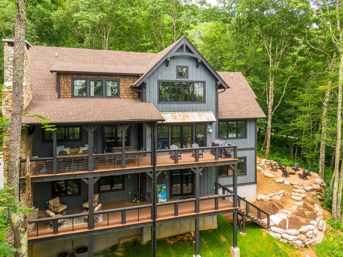 A sweeping multi-level deck overlooking lush greenery, with a fire pit area and expansive windows hinting at the stylish interiors within. The deck is perfectly positioned for sunset views and stargazing, encouraging connection with the mountain surroundings.