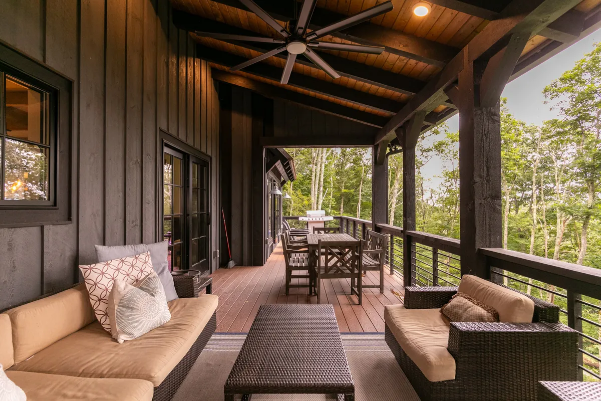 An inviting outdoor seating area features a wooden dining table and plush chairs surrounded by lush greenery. The relaxed setting is perfect for dining, reading, or simply soaking in the natural scenery, embodying the idea of tranquil balconies and decks.