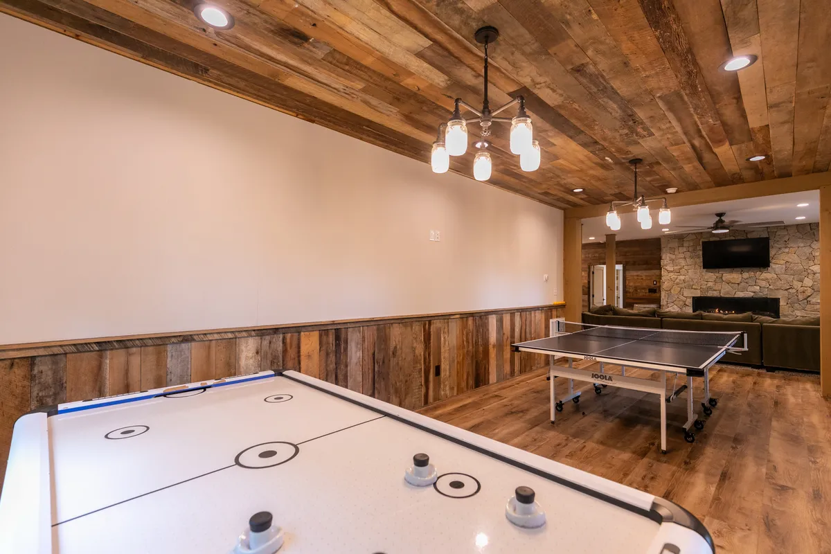 A lively game room equipped with both ping pong and air hockey tables set beneath hanging light fixtures, alongside a stone fireplace. The space is ideal for friendly competition, family tournaments, and energetic gatherings.