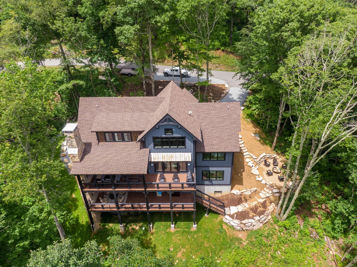 A spacious deck with comfortable seating and a dedicated fire pit area, surrounded by lush greenery. Architectural details of the house are visible, and the setting invites gatherings, relaxation, and enjoying the outdoors from the comfort of the retreat.