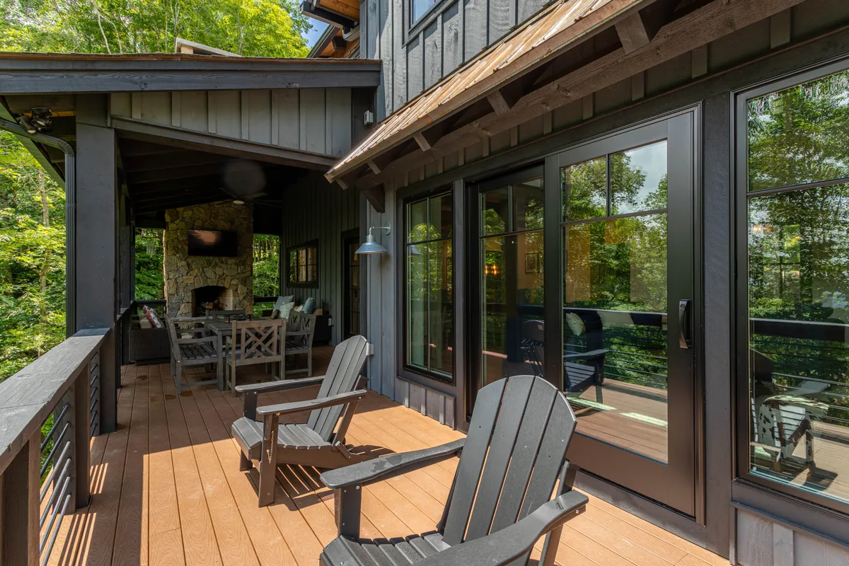 An inviting outdoor space with black Adirondack chairs facing a stone fireplace and large glass doors opening to the greenery. The area blends comfort and natural beauty, ideal for relaxing outdoors or enjoying a warm fire in the evening.