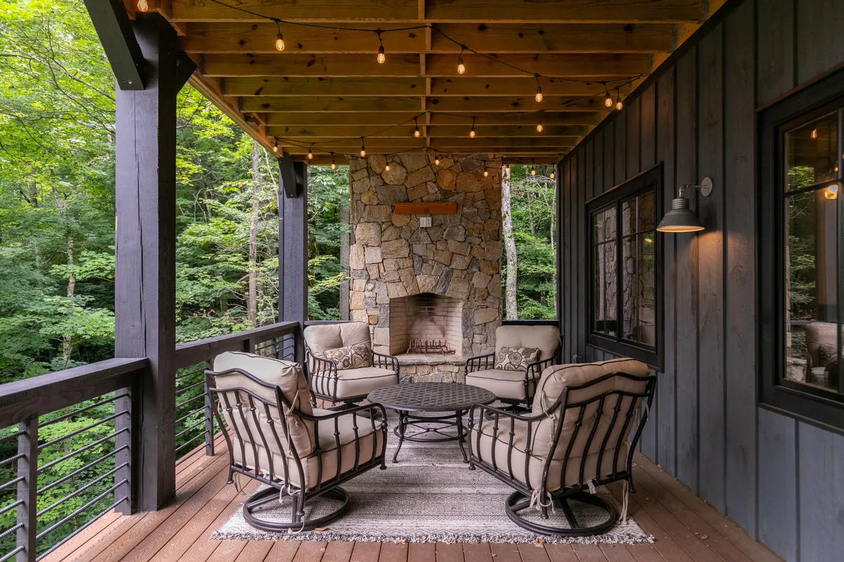 A cozy exterior seating area featuring a stone fireplace, chairs arranged for socializing, and twinkling hanging lights, all nestled among the trees. The mood is tranquil and inviting, perfect for relaxing or sharing stories after a day outside.