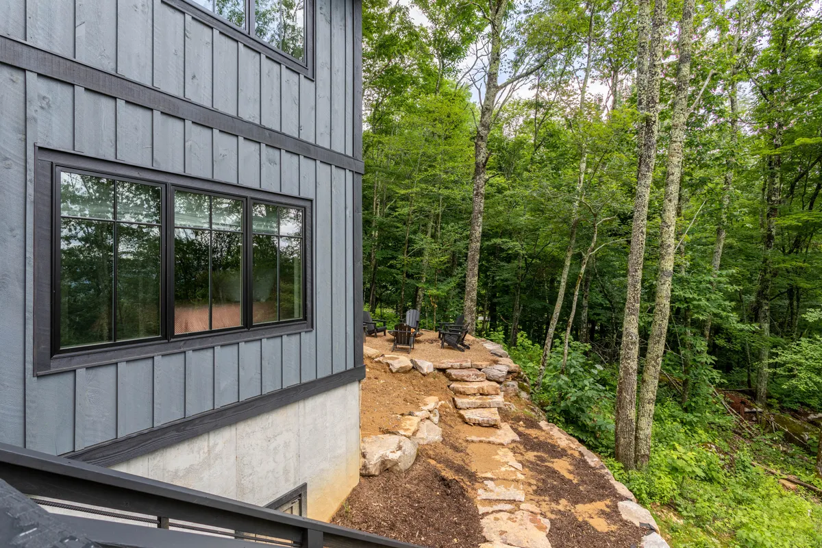 A peaceful wooden deck set among the trees, featuring a rock pathway, comfortable seating area, and lush greenery. The scene is tranquil and invites relaxation or a break outdoors, with nature visible all around.